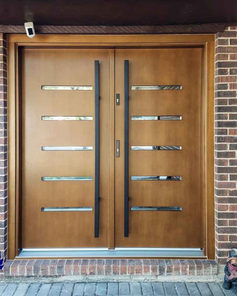 Wood main door in a double door design with metal bar handle, locksets, and a CCTV camera just above the door head
