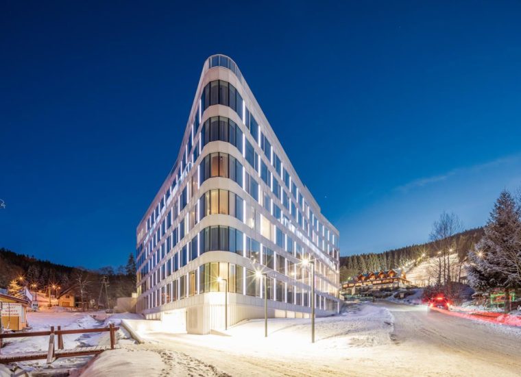 A well-lit hotel building in a triangular form of architecture, standing out in a winter forest background