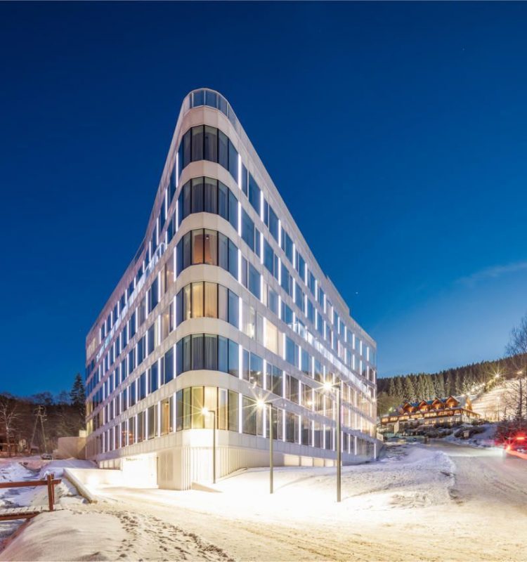 A well-lit hotel building in a triangular form of architecture, standing out in a winter forest background