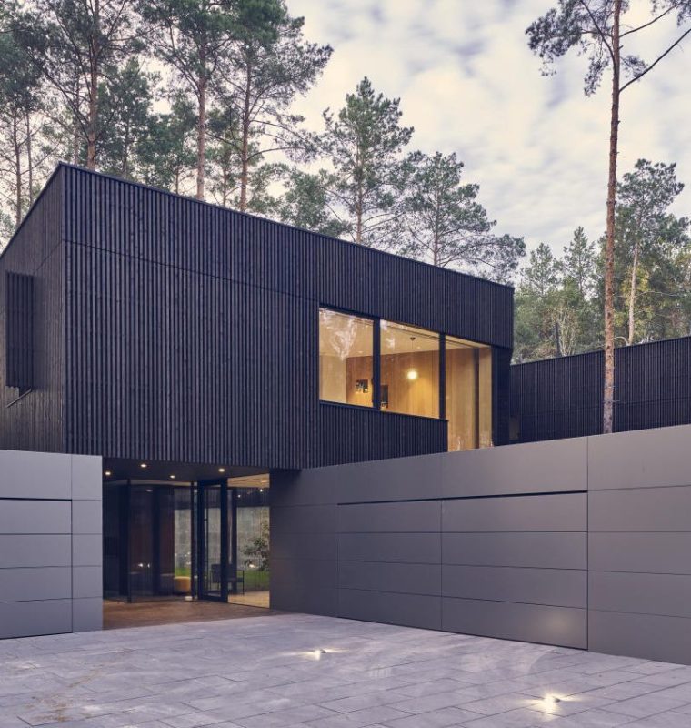 A modern minimalist looking luxurious home with concrete driveway, surrounded by tall trees.