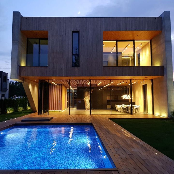 A luxurious home with a well-lit pool, a deck and the architectural style adopting wide glass walls, windows, and door